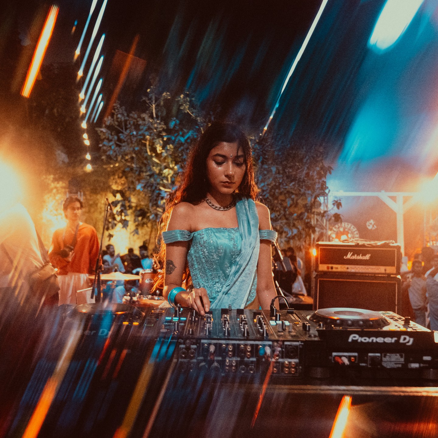 A DJ in blue surrounded by amber and cyan light streaks, photographed by Rafftee Rahman.