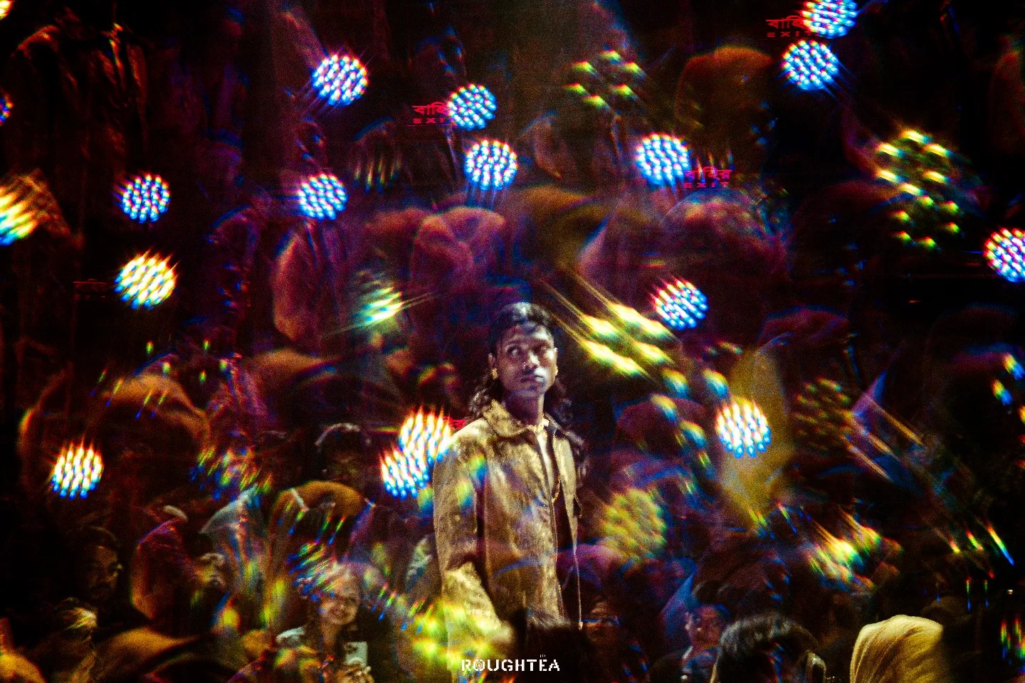 A concert performer framed by a kaleidoscope of multicolored stage lights and audience reflections.